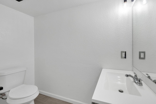 bathroom featuring toilet, baseboards, wood finished floors, and vanity