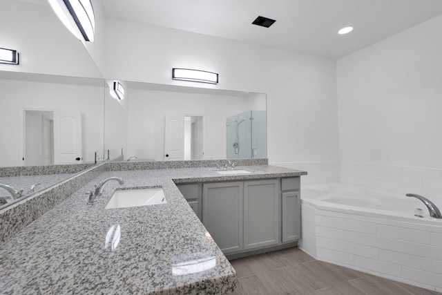 full bath with double vanity, a bath, a sink, and wood finish floors