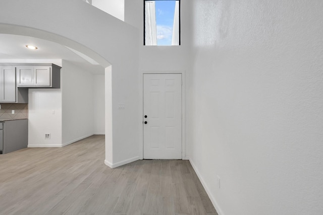 foyer featuring light wood-style flooring, a high ceiling, arched walkways, and baseboards