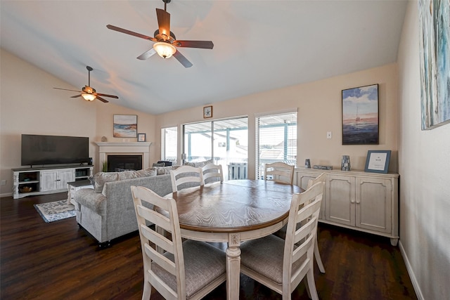 dining room with lofted ceiling, a fireplace, a ceiling fan, baseboards, and dark wood finished floors