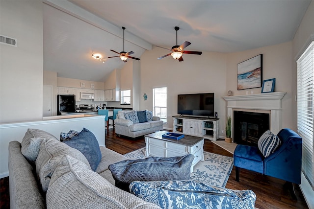 living area featuring visible vents, dark wood-type flooring, a glass covered fireplace, high vaulted ceiling, and beamed ceiling