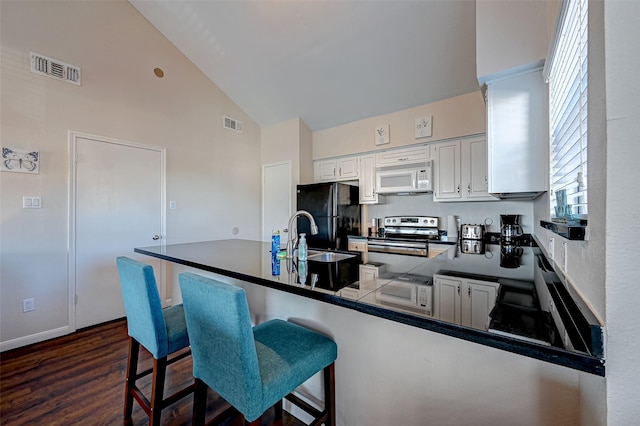 kitchen with dark countertops, white microwave, freestanding refrigerator, stainless steel range with electric stovetop, and white cabinetry