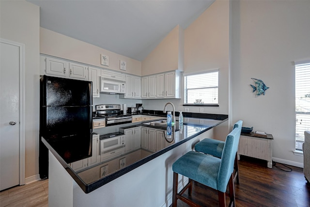 kitchen with dark countertops, electric range, white microwave, white cabinetry, and a peninsula