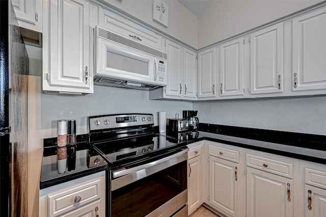 kitchen featuring white microwave, white cabinets, electric stove, freestanding refrigerator, and dark countertops