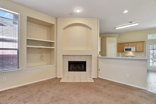 unfurnished living room featuring built in shelves, baseboards, a tiled fireplace, and light colored carpet