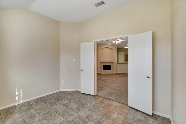 carpeted spare room with lofted ceiling, visible vents, baseboards, a ceiling fan, and a tiled fireplace