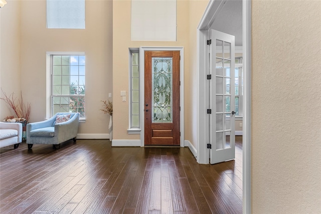 foyer entrance with a towering ceiling, dark wood-style floors, baseboards, and a textured wall