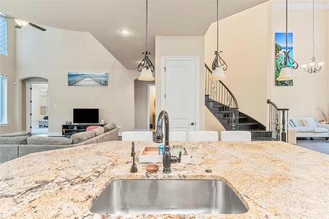 kitchen featuring open floor plan, light stone counters, a sink, and pendant lighting