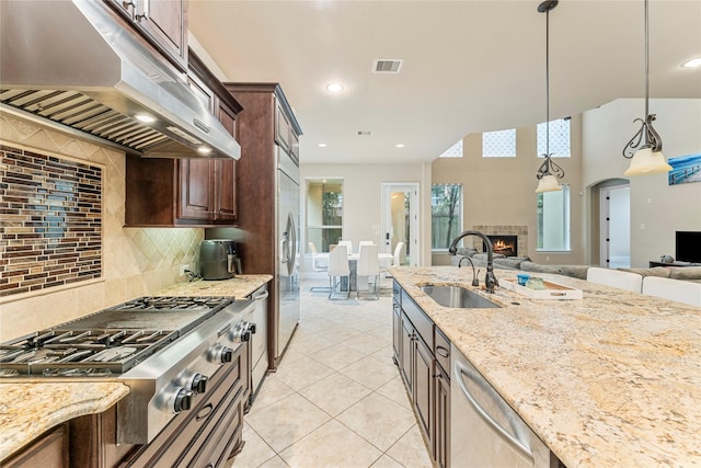 kitchen featuring a warm lit fireplace, under cabinet range hood, a sink, open floor plan, and pendant lighting