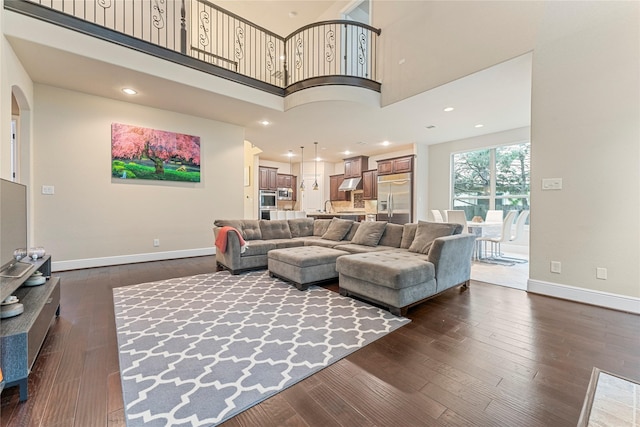 living area featuring dark wood-type flooring, arched walkways, a high ceiling, and baseboards