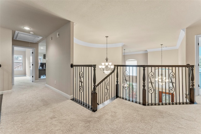 hall featuring attic access, baseboards, an inviting chandelier, crown molding, and carpet floors