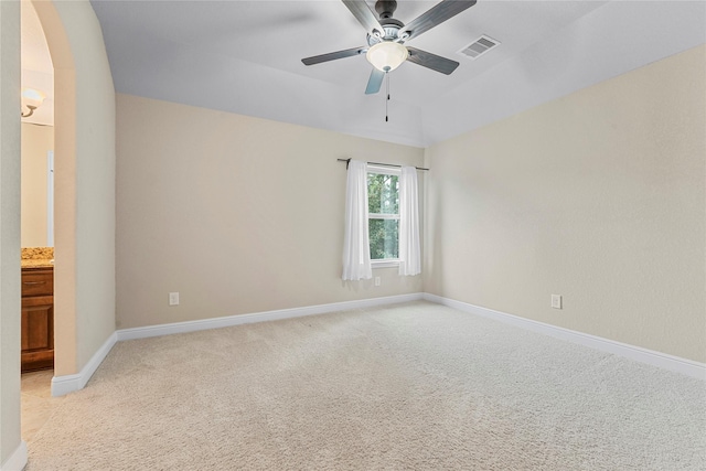 spare room with arched walkways, light colored carpet, a ceiling fan, baseboards, and visible vents