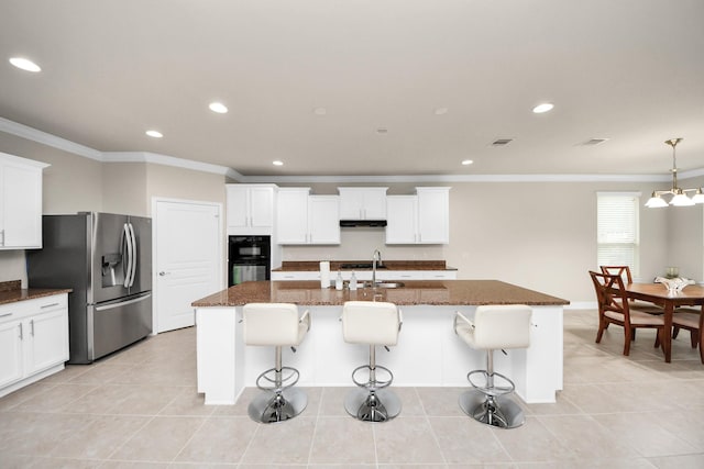 kitchen with an island with sink, dark stone countertops, and stainless steel fridge