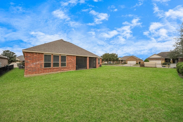 rear view of property featuring roof with shingles, brick siding, a lawn, and fence