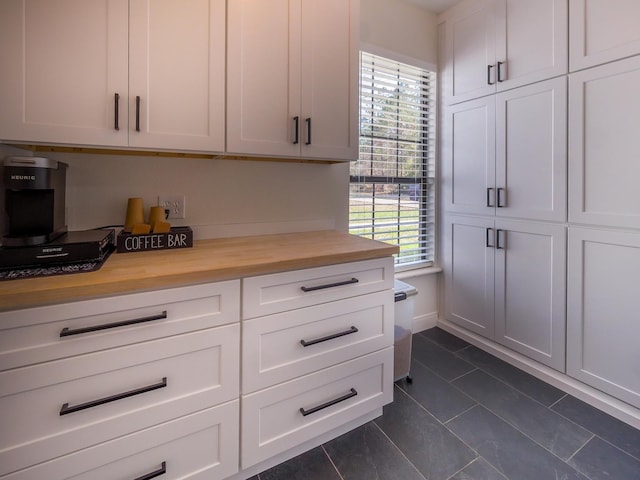 kitchen with dark tile patterned floors, butcher block counters, and white cabinetry