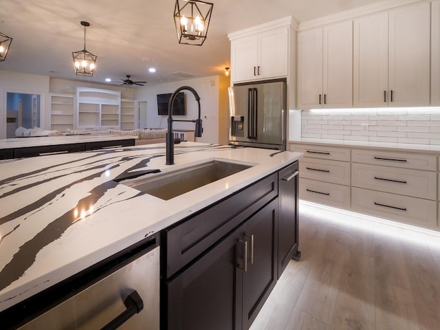 kitchen featuring stainless steel appliances, a sink, white cabinets, open floor plan, and pendant lighting