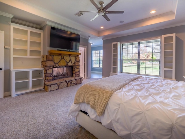 bedroom with carpet, a raised ceiling, visible vents, ornamental molding, and a stone fireplace