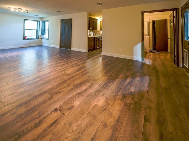 unfurnished living room with dark wood-style flooring, visible vents, and baseboards