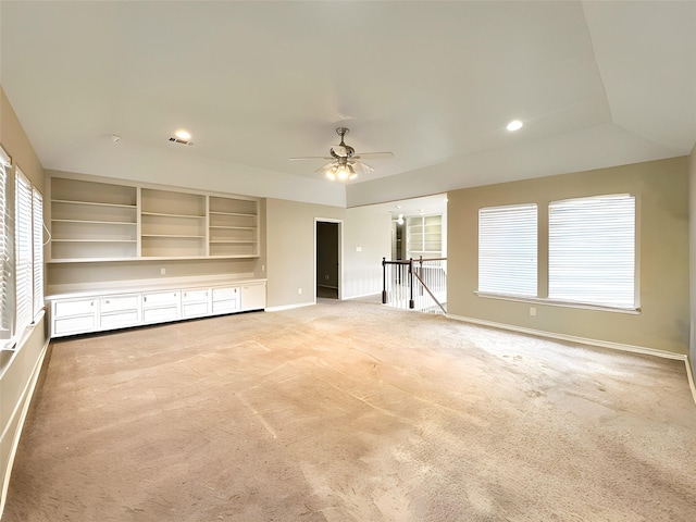 unfurnished living room with a ceiling fan, a raised ceiling, light carpet, and baseboards