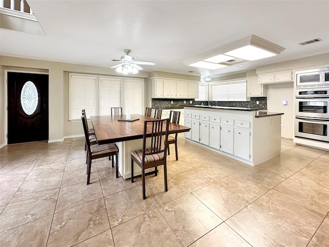 dining area with light tile patterned floors, visible vents, ornamental molding, a ceiling fan, and baseboards