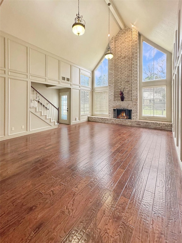 unfurnished living room with hardwood / wood-style flooring, a healthy amount of sunlight, high vaulted ceiling, a decorative wall, and beam ceiling