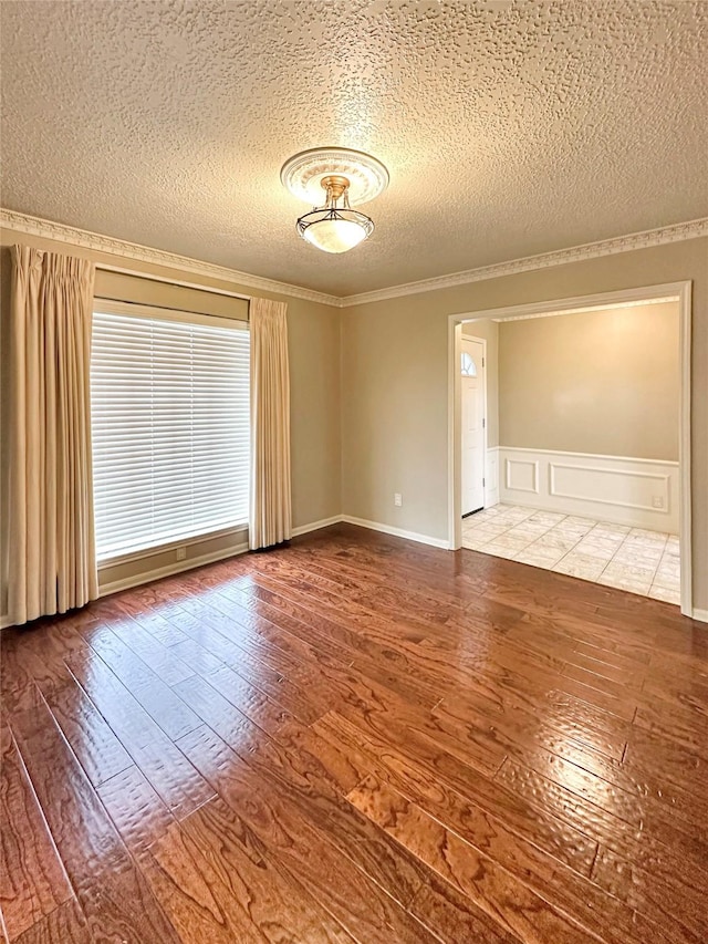 empty room with a textured ceiling, ornamental molding, wood-type flooring, and a decorative wall