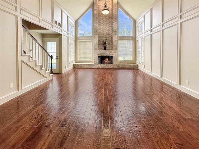 17439 Fairway Oaks Dr, Spring, TX 77379 - unfurnished living room with dark wood finished floors, high vaulted ceiling, a brick fireplace, stairway, and baseboards