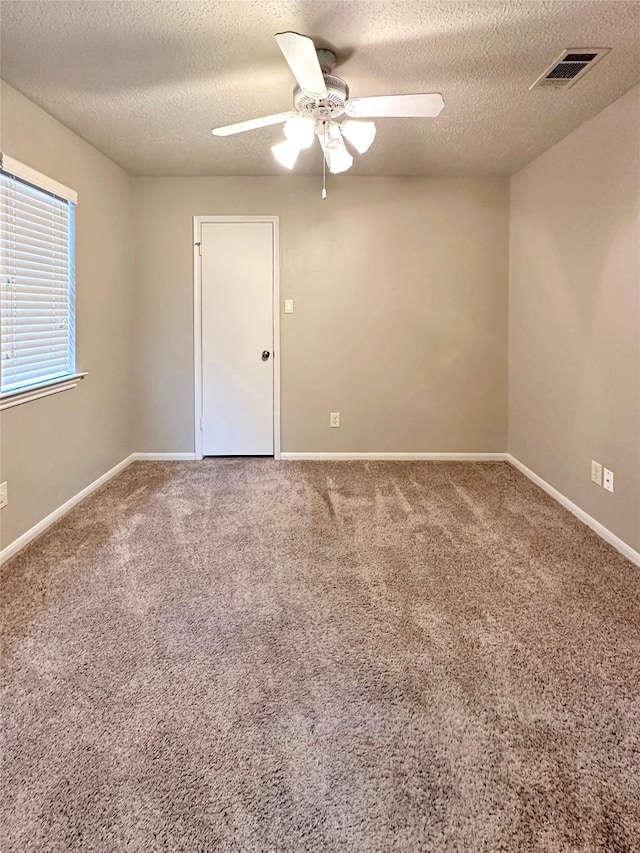 carpeted spare room featuring baseboards, a textured ceiling, visible vents, and a ceiling fan