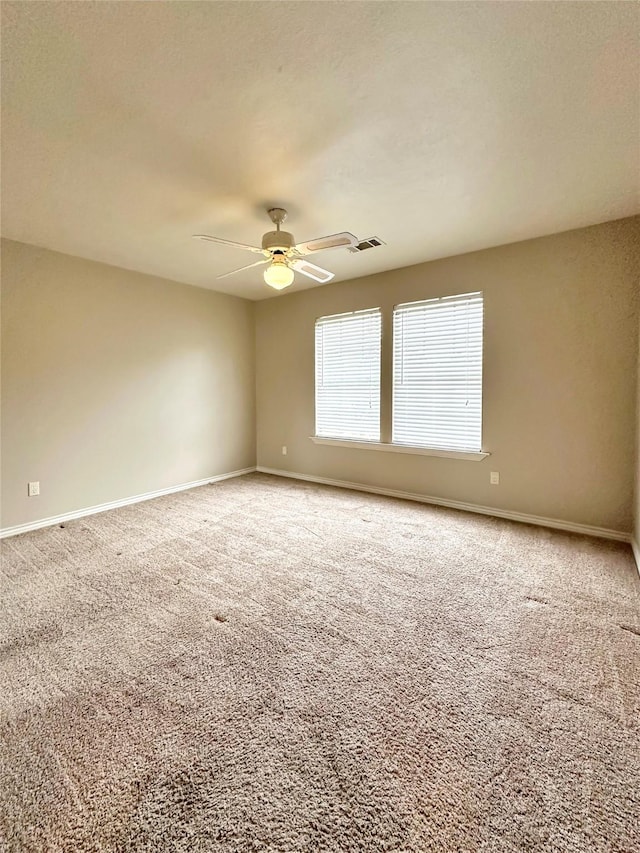 carpeted spare room featuring visible vents, a ceiling fan, and baseboards