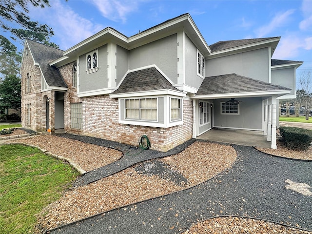 view of front of home featuring a shingled roof, a ceiling fan, stucco siding, a patio area, and brick siding