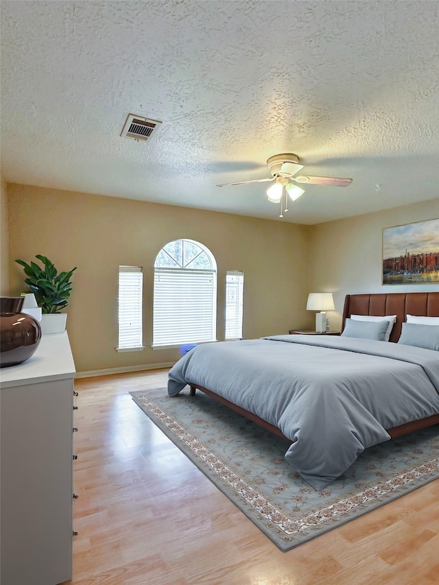 bedroom featuring a textured ceiling, light wood-type flooring, visible vents, and a ceiling fan