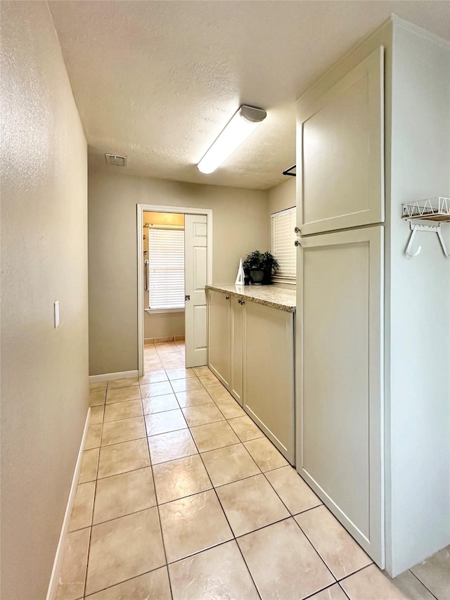 corridor with light tile patterned floors, baseboards, visible vents, and a textured ceiling