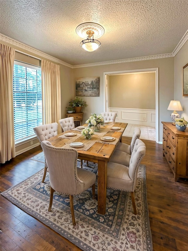 dining room with crown molding, wood-type flooring, a decorative wall, wainscoting, and a textured ceiling