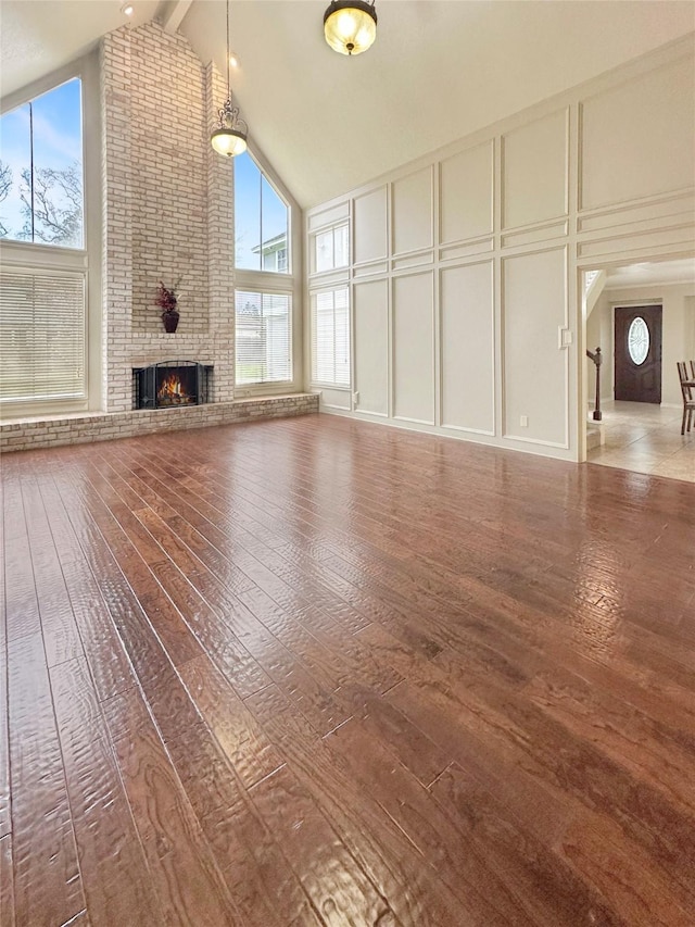 unfurnished living room with high vaulted ceiling, a decorative wall, a brick fireplace, beamed ceiling, and wood-type flooring