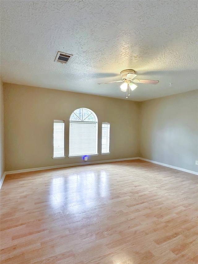 empty room featuring light wood-style floors, ceiling fan, visible vents, and baseboards