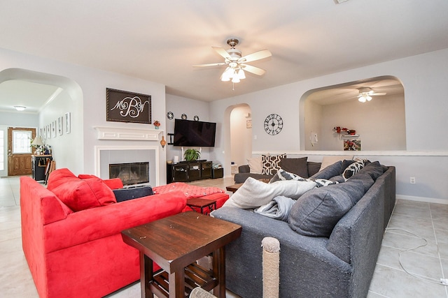 living area featuring arched walkways, a tile fireplace, a ceiling fan, and baseboards