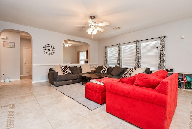 living room with arched walkways, light tile patterned floors, visible vents, a ceiling fan, and baseboards