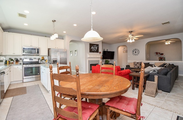 dining area with light tile patterned floors, visible vents, a fireplace, and arched walkways