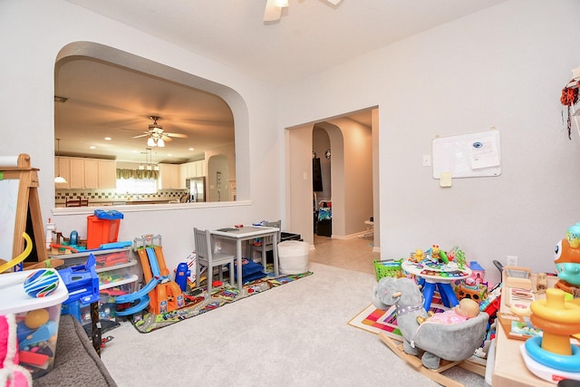 playroom with a ceiling fan, arched walkways, light colored carpet, and light tile patterned floors