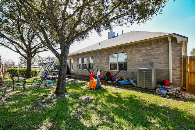 back of property featuring central AC unit, a lawn, a chimney, a playground, and brick siding