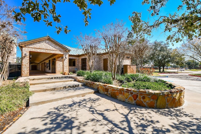 view of front of house featuring a standing seam roof, fence, metal roof, and brick siding