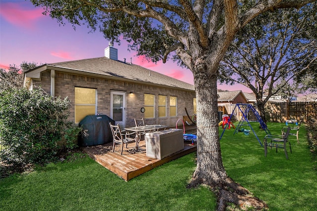 back of property at dusk with a chimney, fence, a lawn, and a playground