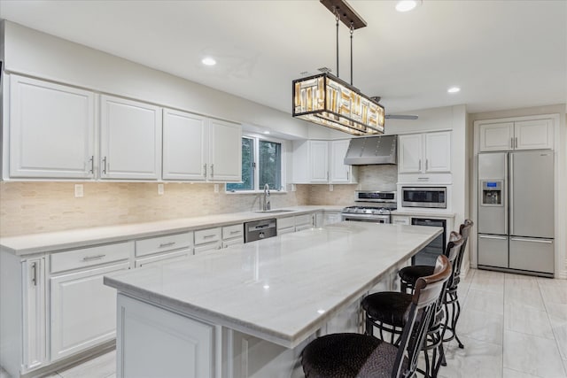 kitchen featuring white cabinets, wall chimney exhaust hood, appliances with stainless steel finishes, a center island, and hanging light fixtures