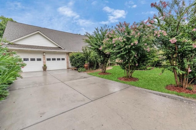 view of front of house featuring driveway, an attached garage, a front lawn, and a shingled roof