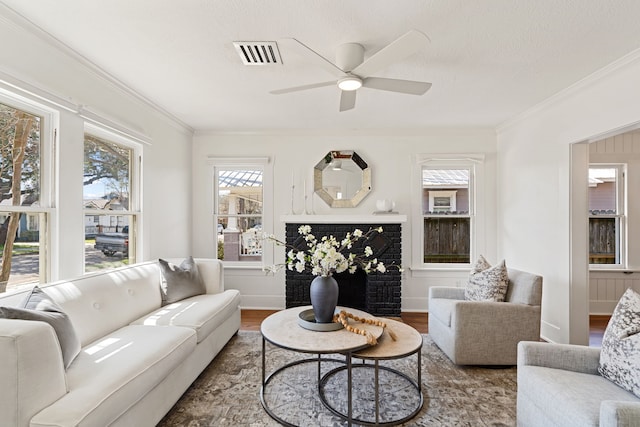 living room featuring a textured ceiling, wood finished floors, a ceiling fan, visible vents, and crown molding