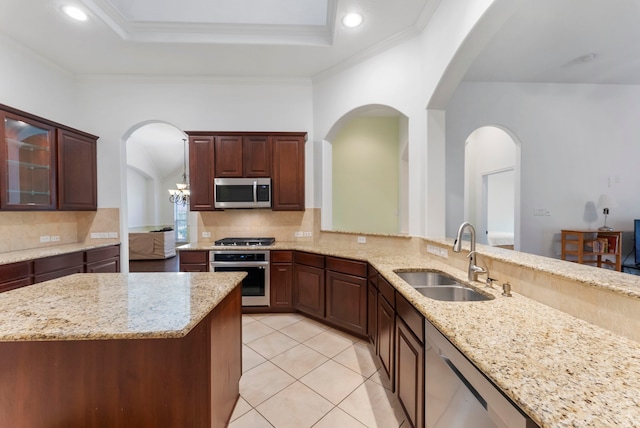 kitchen featuring light stone counters, a tray ceiling, stainless steel appliances, glass insert cabinets, and a sink