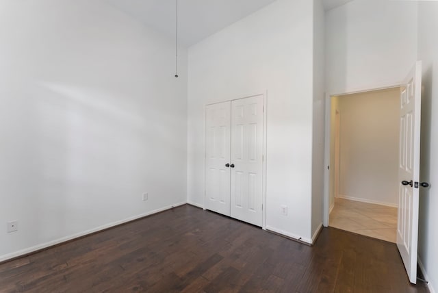 unfurnished bedroom with a towering ceiling, dark wood-style floors, baseboards, and a closet