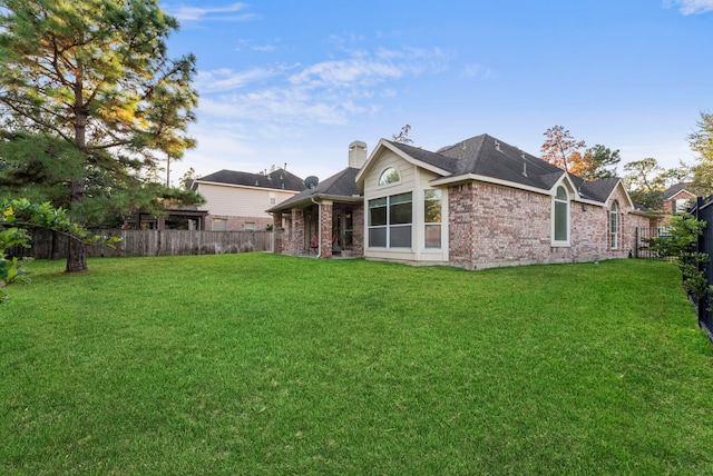 rear view of house featuring a yard, a fenced backyard, brick siding, and a chimney