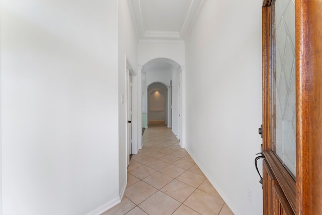 hallway with light tile patterned floors, baseboards, ornamental molding, and arched walkways