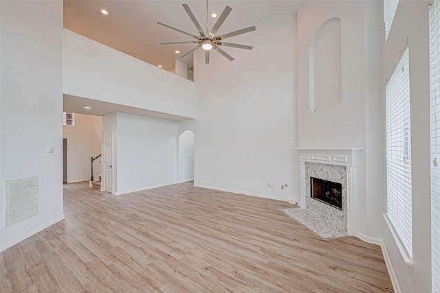 unfurnished living room with a high ceiling, a fireplace, visible vents, and light wood-style floors